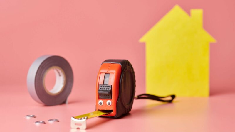 A roll of tape, and a tape measure next to a house shape