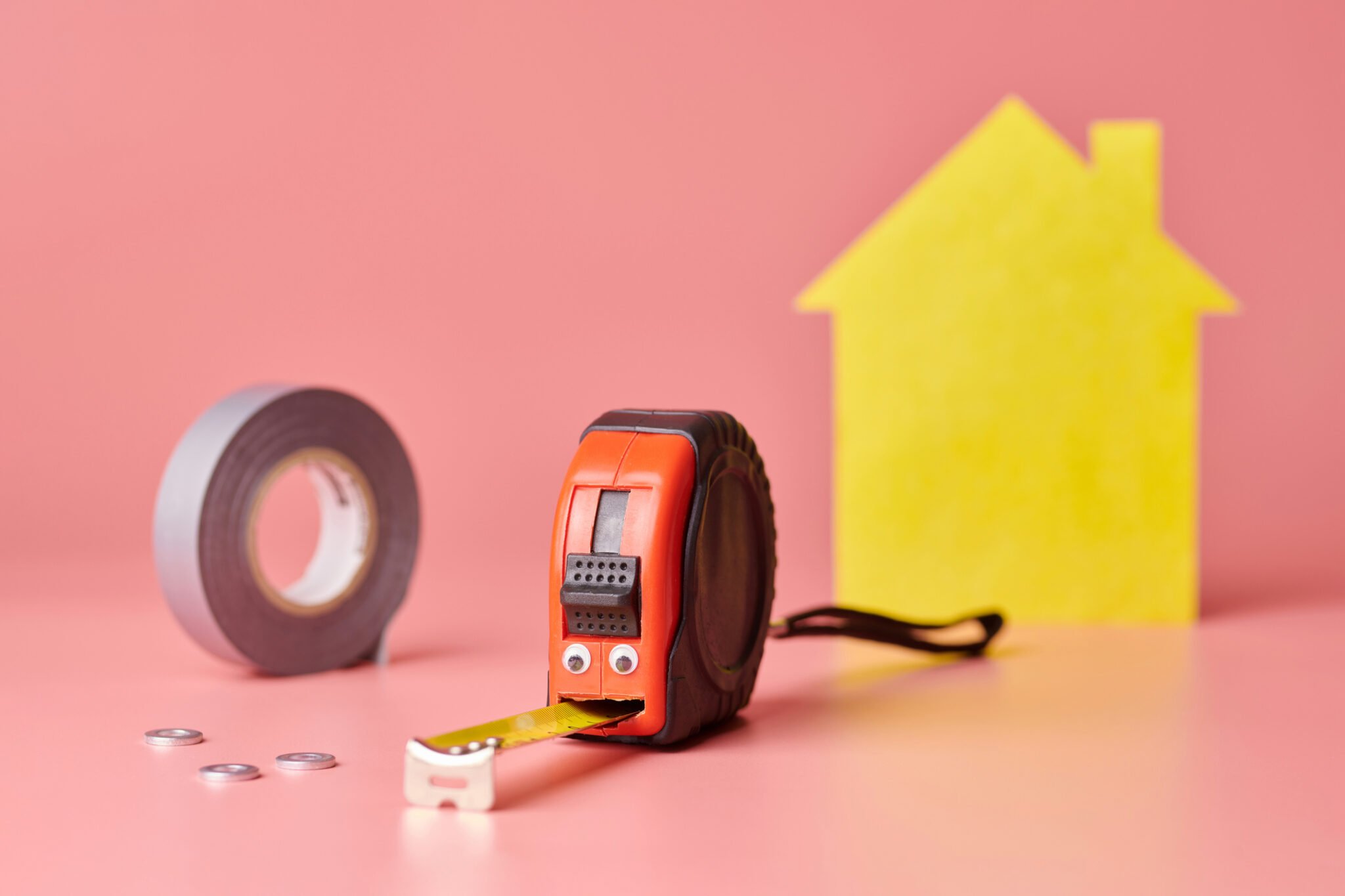 A roll of tape, and a tape measure next to a house shape